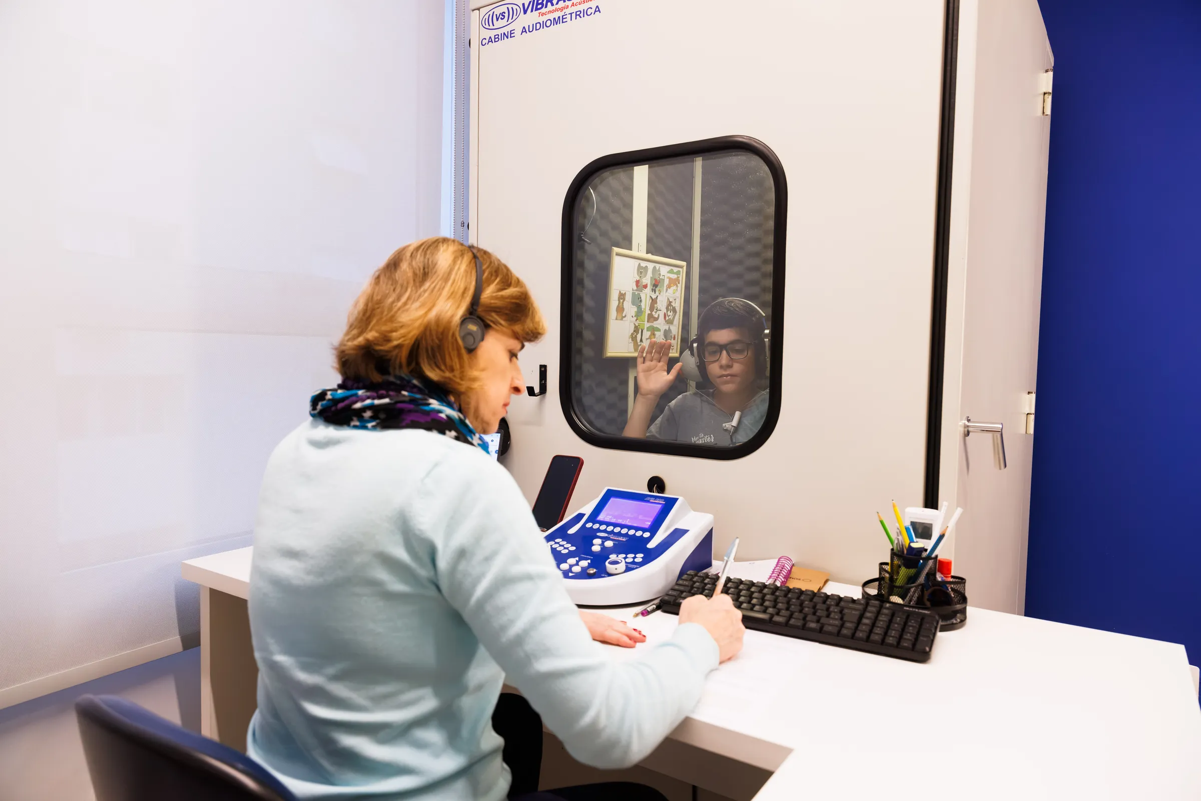 Paciente respondendo ao teste dentro da cabine, visto da mesa do audiômetro