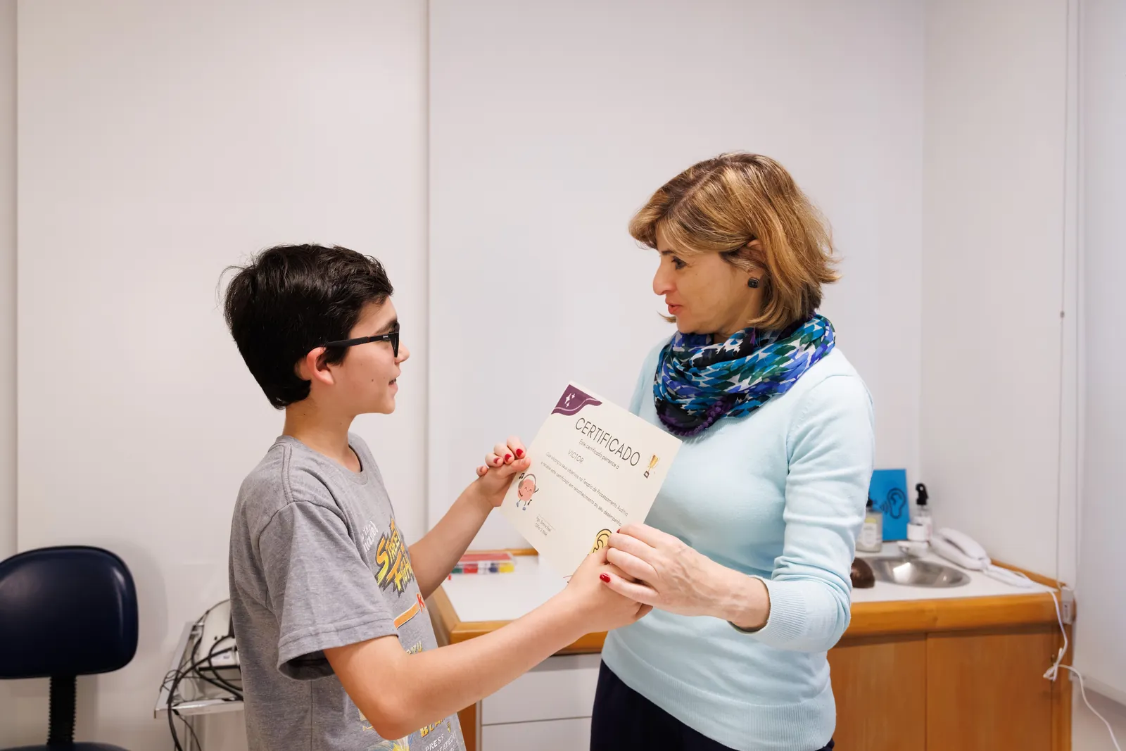 Simone entregando ao paciente o certificado de conclusão do treinamento auditivo